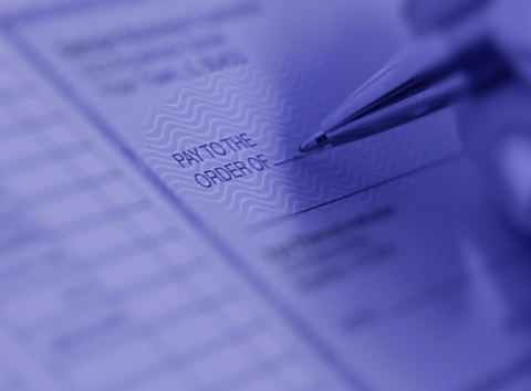 A close-up of a hand holding a pen over a modern, professionally designed check, focusing on the &ldquo;Pay to the Order Of&rdquo; section with subtle security patterns and a clean, polished layout.